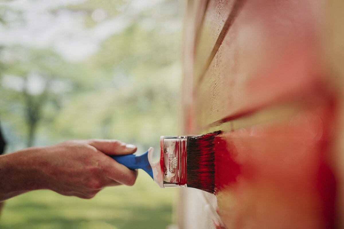 Kuvassa on pensselillä punaista ulkoseinää maalaava käsi.